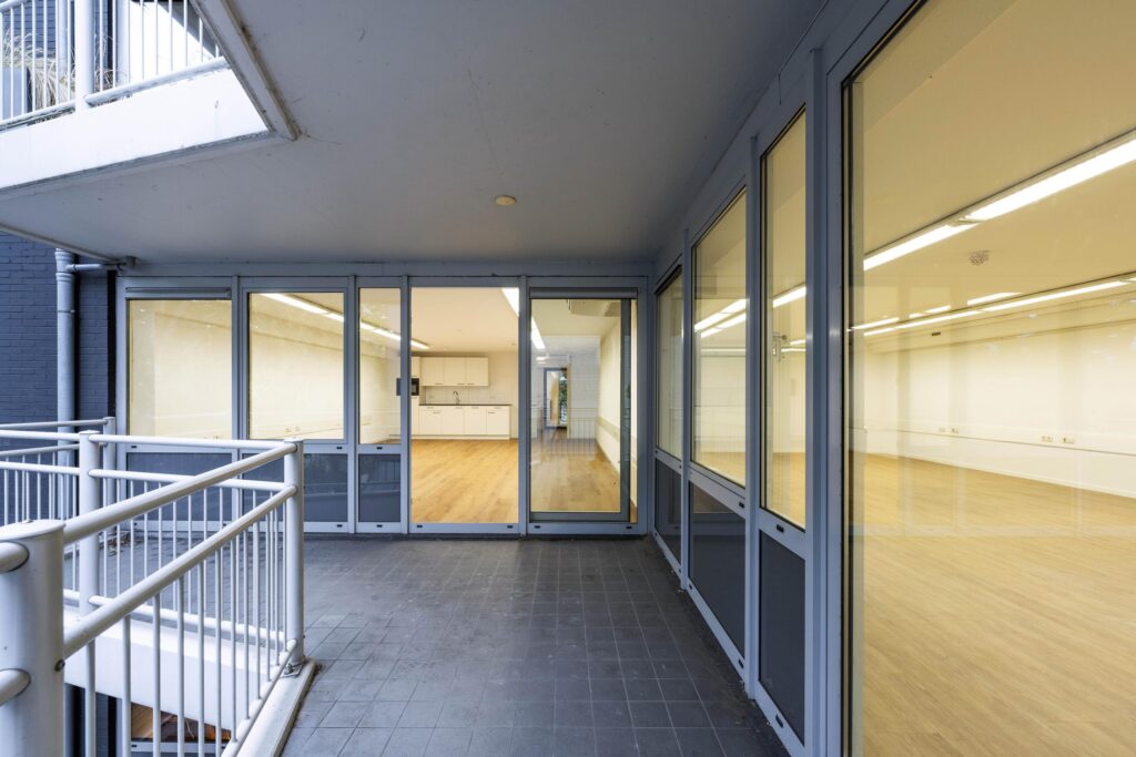 Ingang van een modern, leeg kantoorpand aan de Prins Hendrikkade met glazen schuifdeuren en een houten vloer.